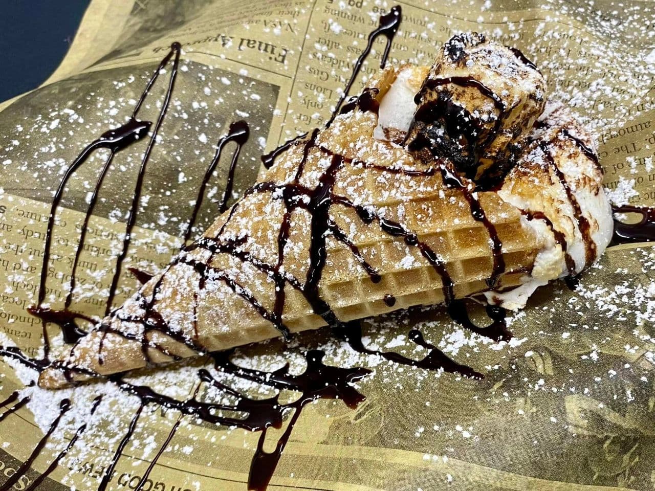 A warm waffle dessert with toasted marshmallow, chocolate drizzle, and powdered sugar.